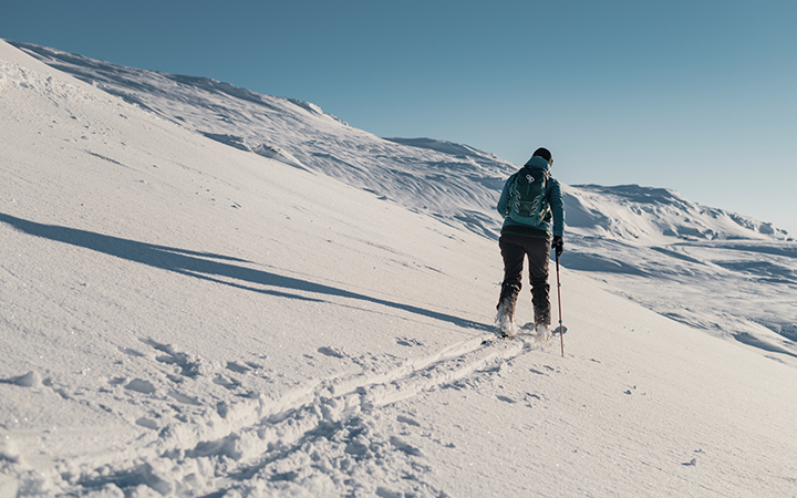 En person vandrar med skidstavar på en snötäckt bergssluttning under en klar himmel