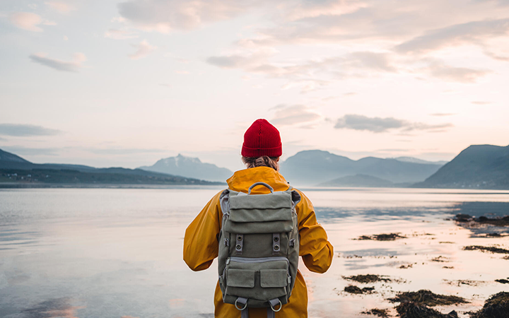 Person med ryggsäck vid sjö i nordisk natur, solnedgång i bakgrunden