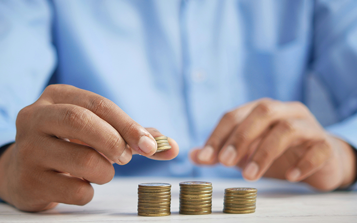 Person räknar mynt och staplar flera högar på ett bord, symboliserar sparande och ekonomi