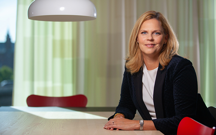 Kvinna med blondt hår i svart kavaj sitter vid ett bord i modernt kontor