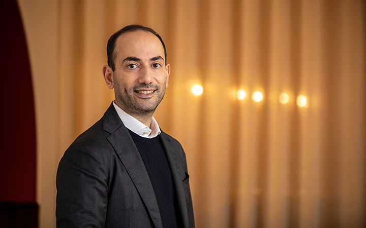 Man i kostym ler mot kameran med varm belysning i bakgrunden