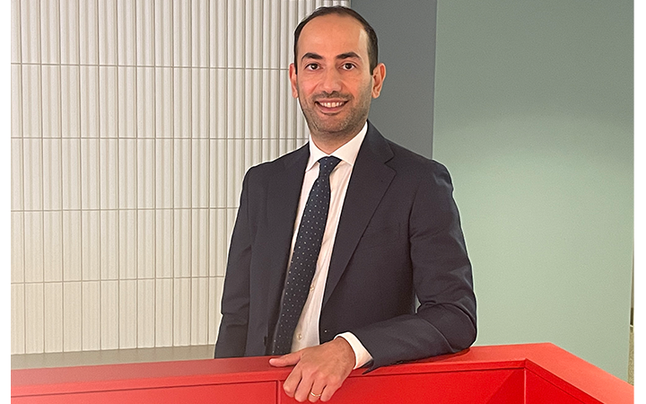 Nadir Hakimi i kostym står vid ett rött skrivbord i ett modernt kontorslandskap