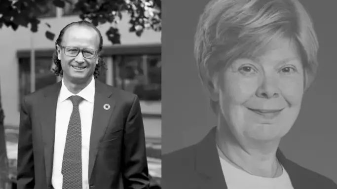 Två personer i affärskläder, en man till vänster med glasögon och slips, och en kvinna till höger i kavaj. Bakgrunden är utomhus med träd och byggnader