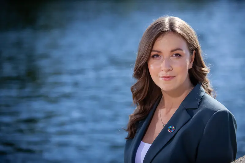 Victoria står utomhus med vatten bakom sig.