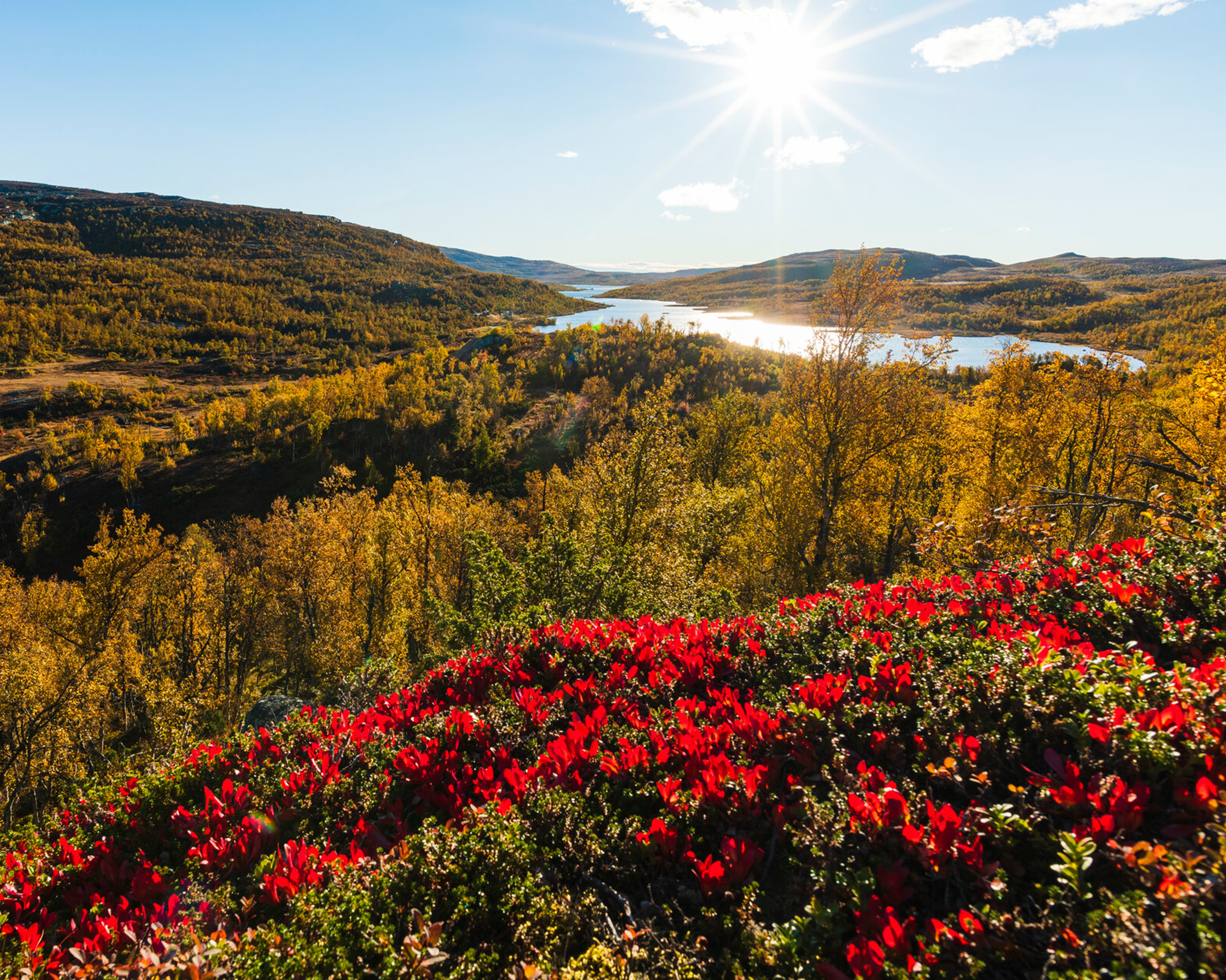 Landskap i höstfärger med solsken, berg och vatten.