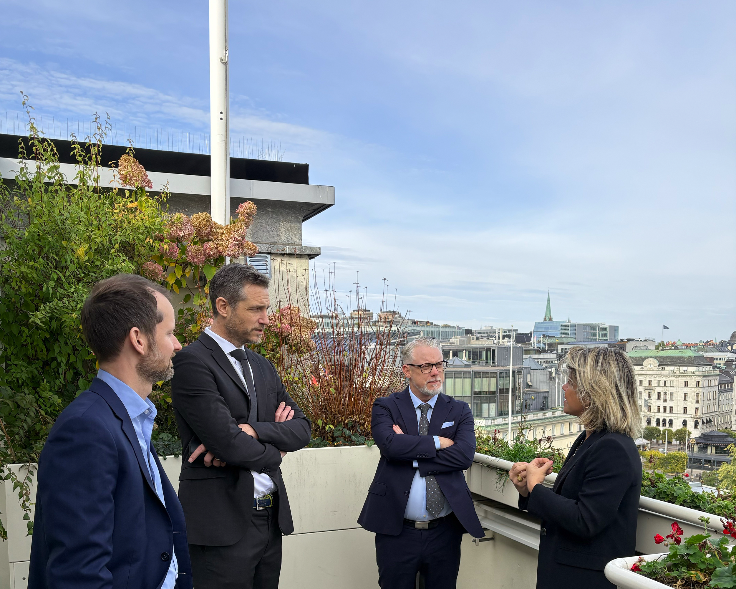 Fyra personer står på en terrass och diskuterar med Stockholm i bakgrunden.