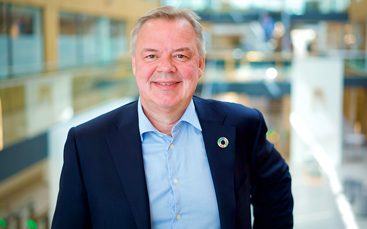 Odd Arild i kostym står i en modern kontorsmiljö och ler mot kameran