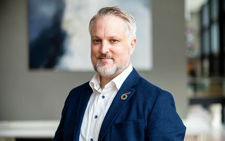 Man i blå kavaj och vit skjorta står framför en suddig bakgrund, ser professionell ut