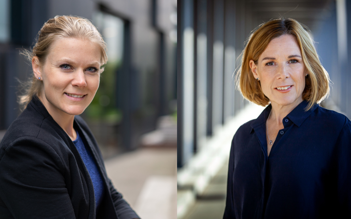 Två kvinnor i affärsmiljö med modern kontorsarkitektur i bakgrunden. De har på sig professionella kläder och ler mot kameran