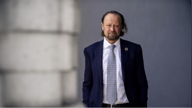 Man i kostym med slips står utomhus mot en grå bakgrund