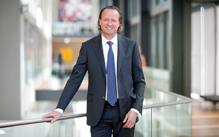 Man i kostym står vid en modern kontorsmiljö, leende och avslappnad