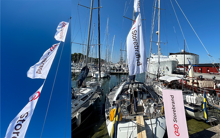 Segelbåtar förtöjda i en hamn under klarblå himmel med flaggor som bär logotypen "Storebrand"