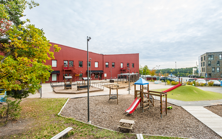 Lekplats med rutschkana och klätterställning framför en röd byggnad i en modern stadsdel