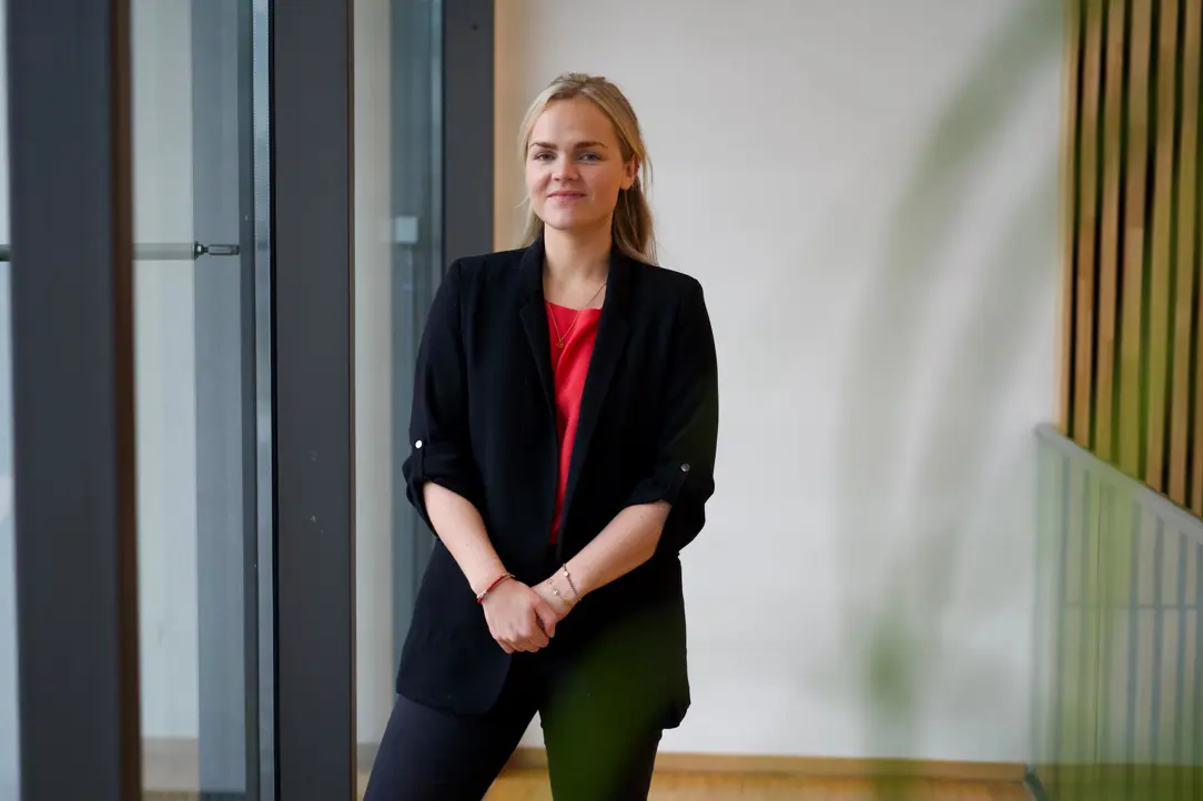 Kvinna i svart kavaj står leende inomhus nära ett glasparti