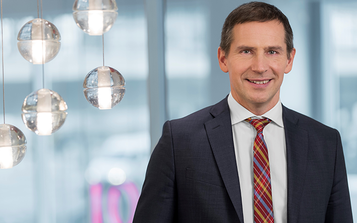 Lars Pettersson i kostym med rutig slips på ett kontor, modernt upplyst interiör i bakgrunden