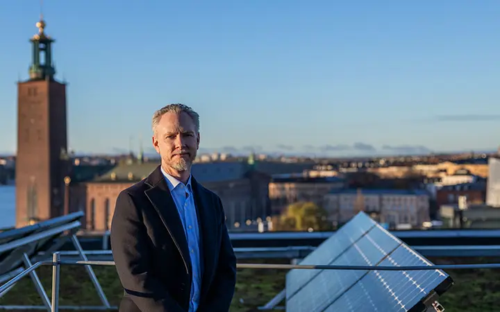 Person som står framför Stockholms Stadshus med solpaneler i fokus, en klar himmel i bakgrunden