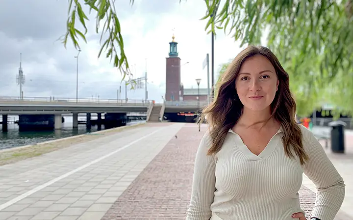 Kvinna framför Stockholms stadshus vid vattnet en molnig dag, Sverige