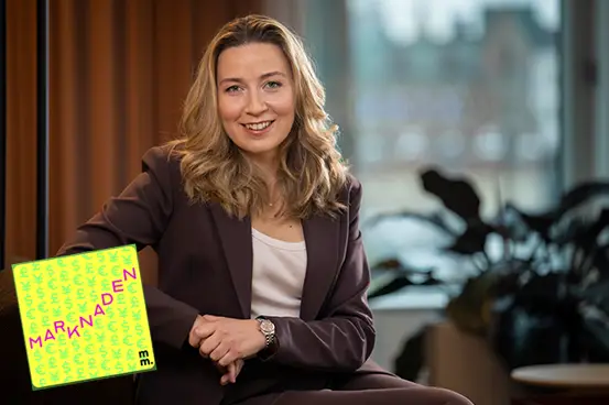 Kvinna i kostym sitter i ett modernt kontor med växter i bakgrunden, marknadsföringsmaterial syns i bild