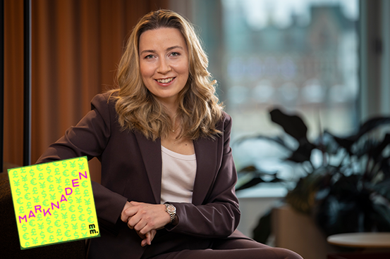 Kvinna i kostym sitter i ett modernt kontor med växter i bakgrunden, marknadsföringsmaterial syns i bild