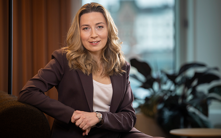 Kvinna i brun kostym sitter på en soffa i ett modernt kontor med växter i bakgrunden