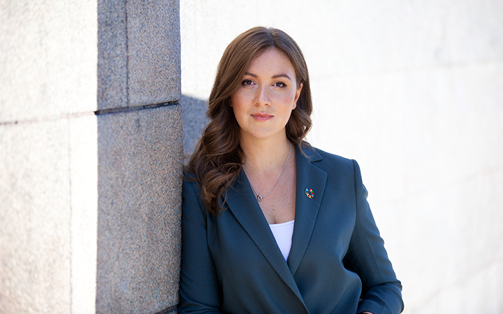 Person i mörk kostym står vid stenmur, tittar mot kameran