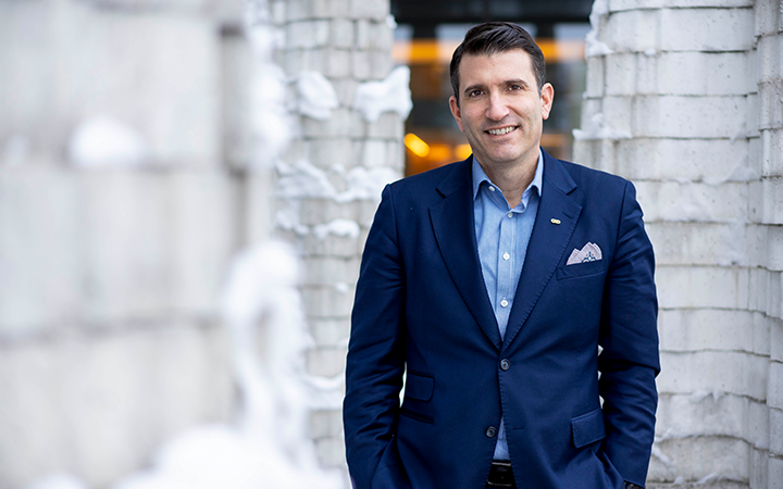 Man i mörkblå kostym står utomhus mot en bakgrund av snö och tegelväggar