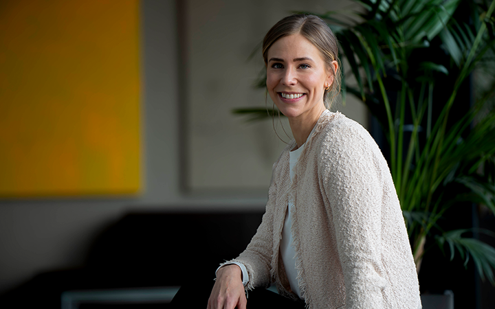 Leende kvinna i en vit tröja sitter i en modern inomhusmiljö med gröna växter i bakgrunden