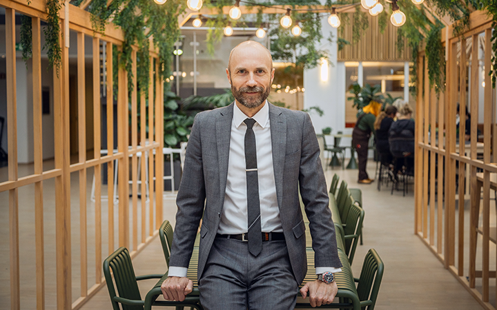 Man i grå kostym står i modernt kontor med trädetaljer och hängande lampor