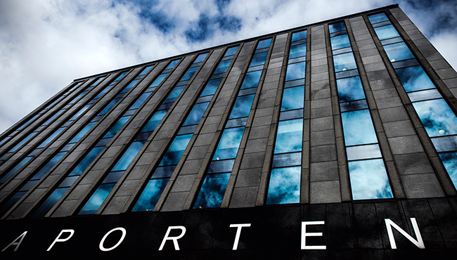 Modern kontorsbyggnad med glasfasad och reflektion av moln på himlen, Stockholm