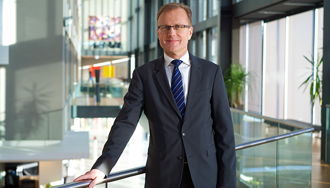 Man i kostym står i en modern kontorsmiljö, hållandes i ett räcke