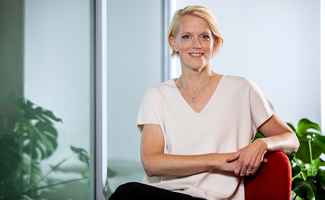 Kvinna i vit blus sitter på röd stol i modernt kontor med gröna växter i bakgrunden