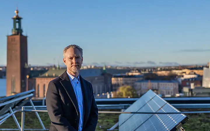 En man i kostym står på ett tak i Stockholm med Stadshuset i bakgrunden. Solpaneler syns i förgrunden