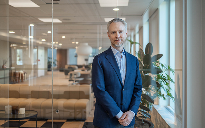 Man i blå kostym står i modernt kontorsutrymme med växter och glasväggar i bakgrunden