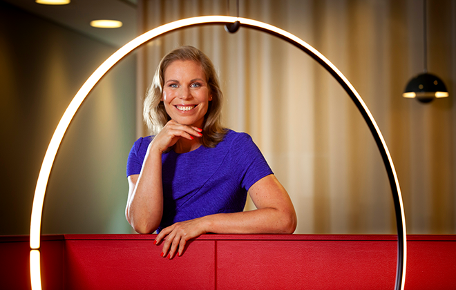 Kvinna i blå klänning ler och poserar bredvid en modern ljusinstallation inomhus