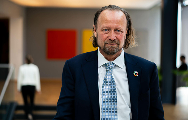 Man i kostym och slips står i modern konstutställning, med abstrakta målningar i bakgrunden