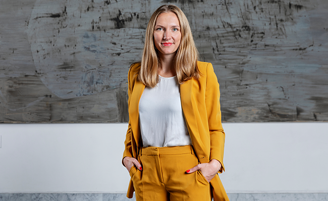 Kvinna i en gul kostym står framför en modern abstrakt målning