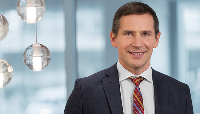 Man i kostym med randig slips i ett modernt kontor, leende mot kameran