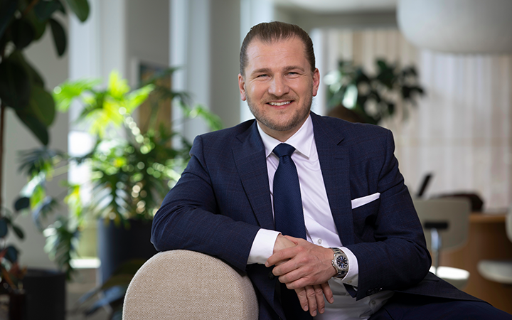 Man i kostym ler i ett kontor med gröna växter i bakgrunden