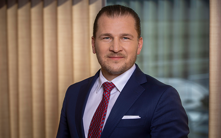 Affärsman i kostym och slips står framför en fönstergardin