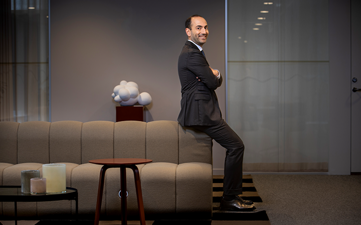Nader Hakimi i kostym står leende vid en soffa i modernt kontor, med designmöbler och dämpad belysning