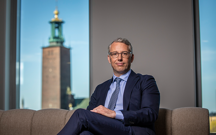 Man i kostym framför ett fönster med utsikt över Stadshuset i Stockholm