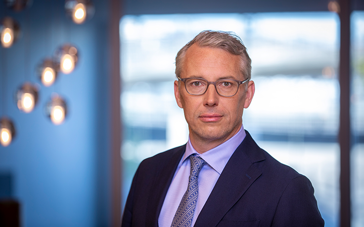Man i kostym och glasögon med moderna lampor i bakgrunden
