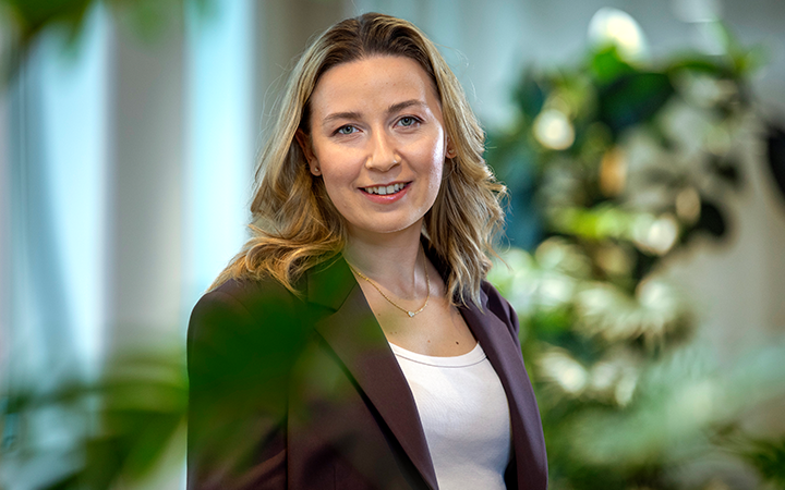 Kvinna i affärskläder ler framför en grönskande bakgrund