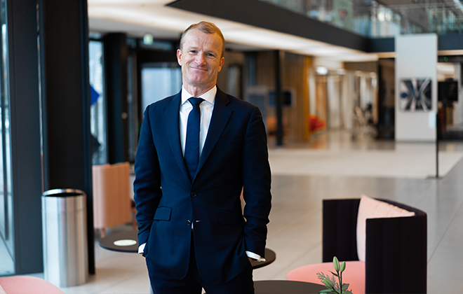 Man i mörk kostym står i modernt kontorslandskap med leende uttryck