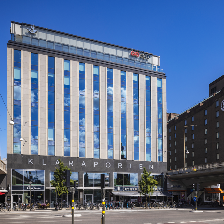 Modern kontorsbyggnad i Stockholm med skyltar för SJ och SPP. Byggnaden har stora glasfönster och himlen reflekteras i fasaden