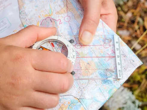 Händer som använder en kompass på en orienteringskarta utomhus