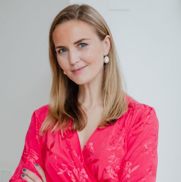 Kvinna i röd klänning med blommönster, leende och stående mot vit bakgrund