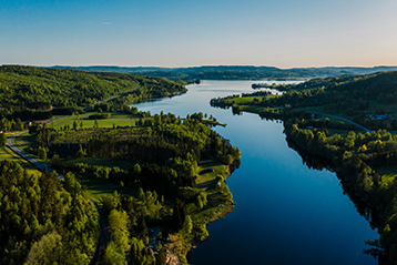 Flygbild av en svensk sjö omgivet av grönskande skogar och ängar