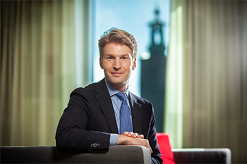 Man i kostym sitter i kontorsmiljö med utsikt över stadslandskap