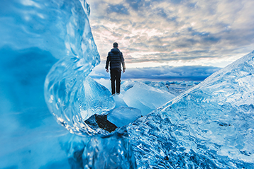 Person står på isblock i ett isigt landskap under molnig himmel